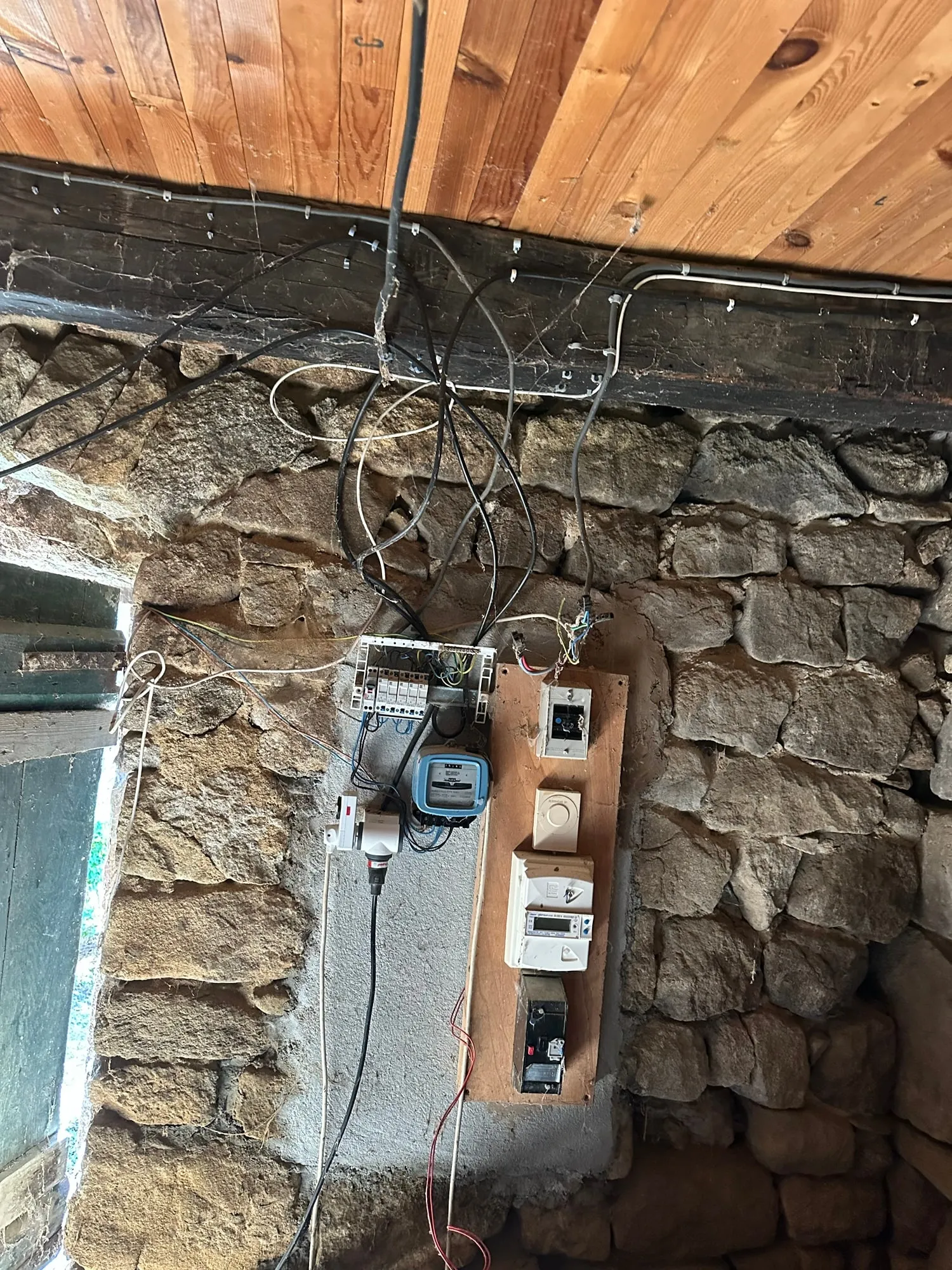 Électricité d’une vieille maison à Aizac avant rénovation : câbles apparents et ancien tableau sous un plafond en bois.