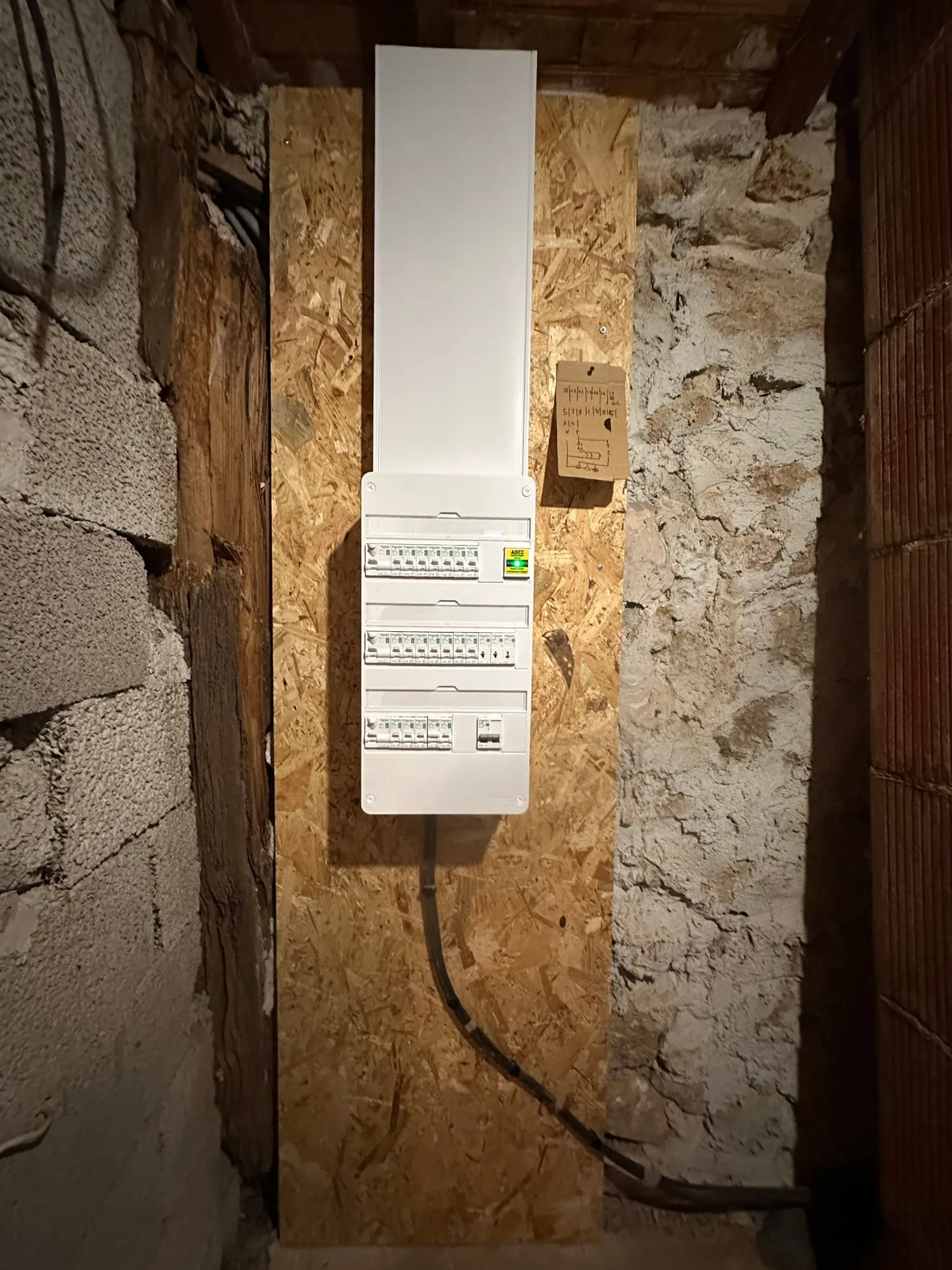 Tableau électrique rénové à Juvinas, avec trois rangées de protections et une goulotte sur un mur en pierre.